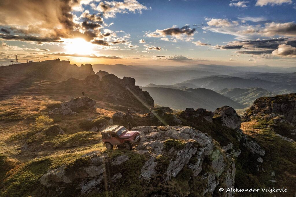 Off-road travel through the mountains - an off-road vehicle drives over rocky paths in the middle of a spectacular mountain landscape at sunset.